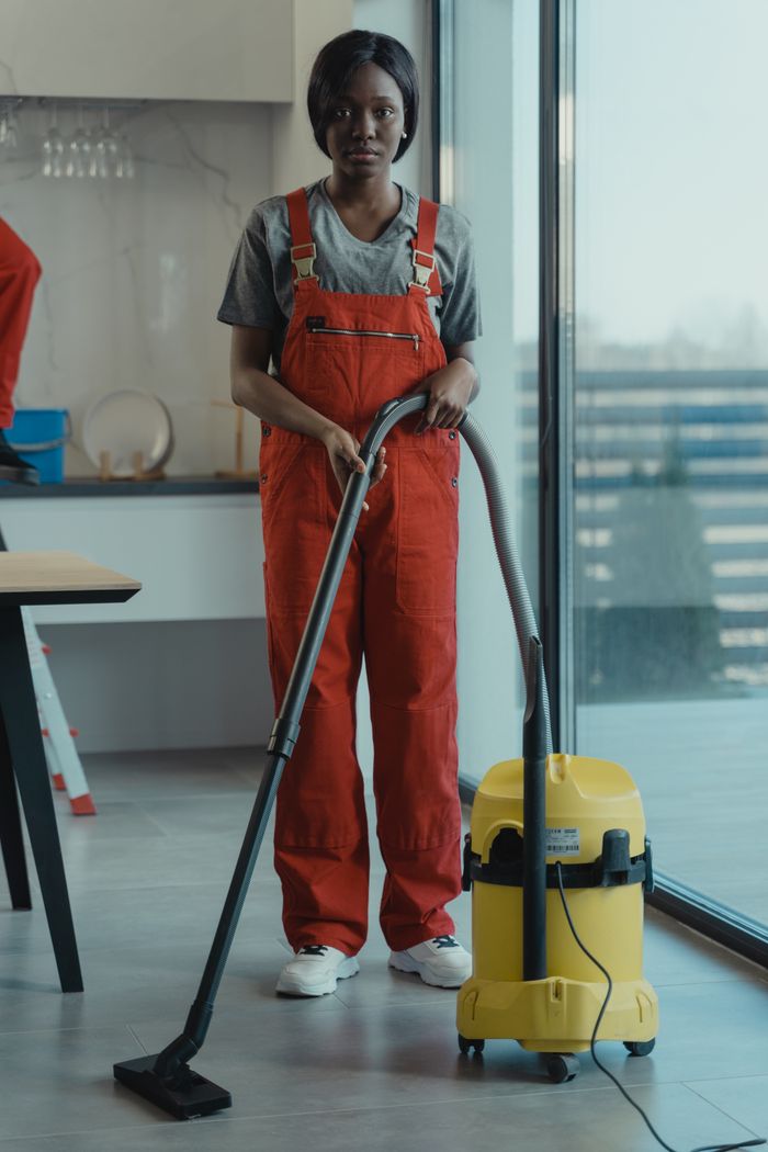 creative-03 Une femme adulte vêtue d'une combinaison rouge utilise un aspirateur dans un intérieur moderne, concentrée sur les tâches de nettoyage.