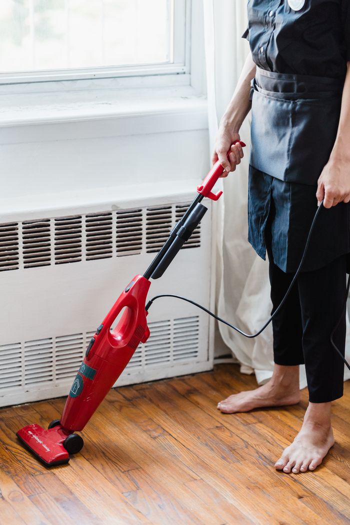 mobile-01 A person vacuuming a wooden floor with a red vacuum cleaner in a brightly lit room.